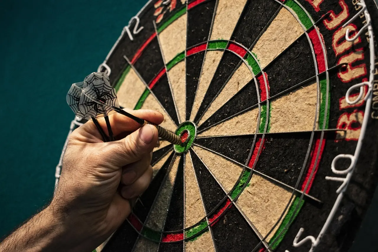 Dartskive med pile og hånd der tager en pil ud